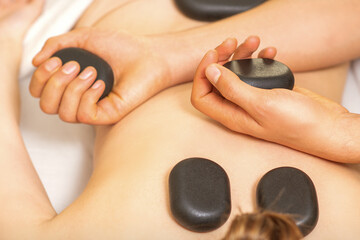 Hot stone massage on the female back with hands of masseur holding black massage stones in spa salon