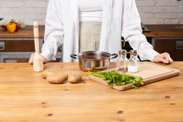 Women cooks potatoes and green in kitchen