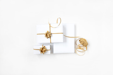Three gift boxes in white wrapping paper with gold ropes on white table. Isolated wrapped gift mock up.