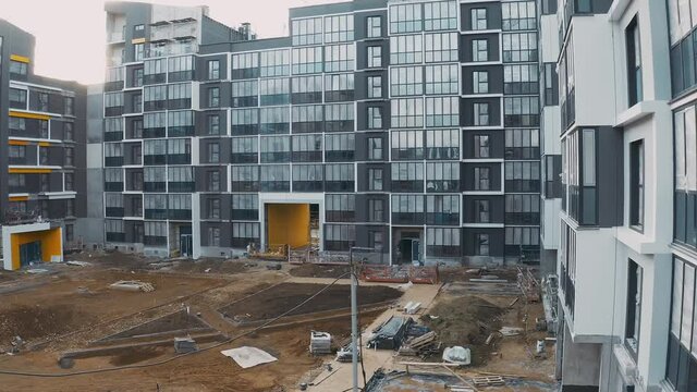 Construction site with scaffold, building work process modern an apartment panel house. Decoration and cladding of facades block of flats. Aerial view of courtyard with sand, yellow arch and porches