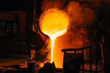 Liquid metal pouring into mold from ladle in foundry metallurgical plant.