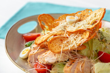 Caesar salad with grilled chicken on white wooden background