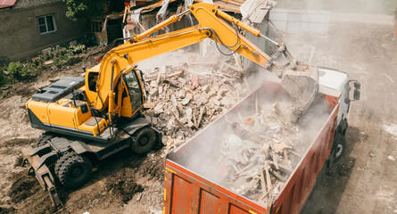 Excavator breaks building and loads construction waste into truck with its bucket. Demolition of...