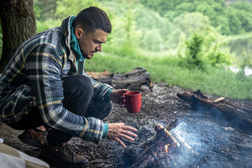 A man on a hike sits by the fire and warms himself.