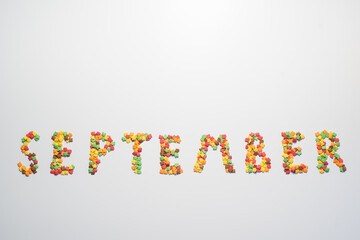 The inscription September on a white background. Confectionery sprinkles in the form of multi-colored maple leaves