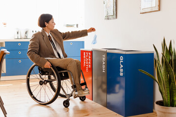 White woman in wheelchair throwing face mask in recycling box at office