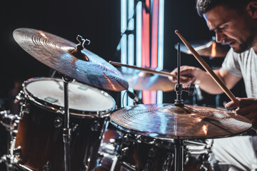 A male drummer plays drums with drum sticks.