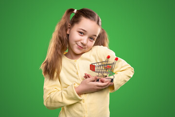 Smiling girl with miniature shopping cart on green background