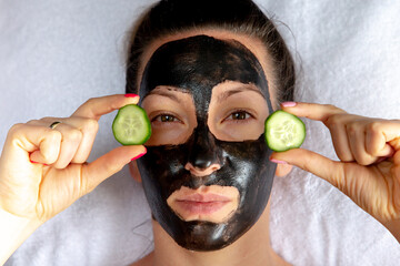 Natural looking girl with black caracol face mask laying on white towel at spa salon