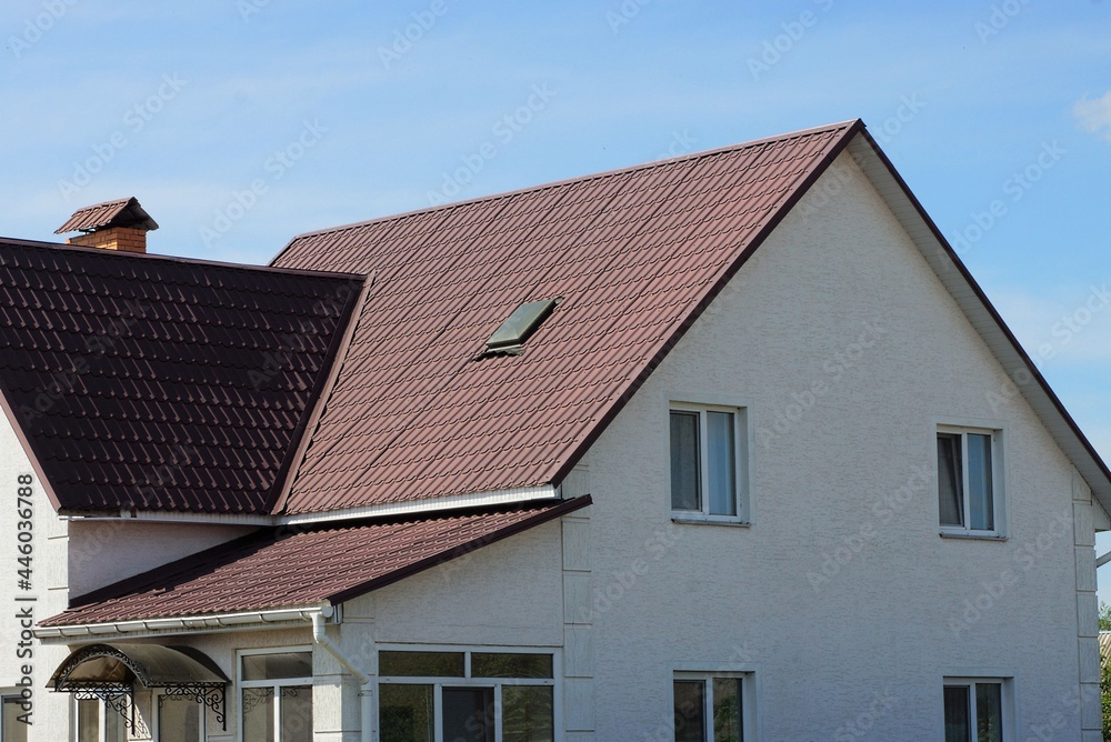 Sticker facade of a large white private house with windows under a brown tiled roof against a blue sky