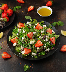 Asparagus and Strawberry Salad with vegetables, green peas and feta cheese in black plate. healthy food.