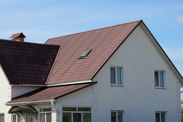 facade of a large white private house with windows under a brown tiled roof against a blue sky