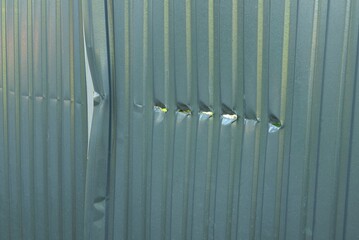 part of a gray metal deformed wall of a fence with a crack and small holes in the street