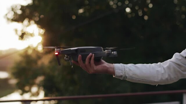 The guy holds a drone in his hand to launch it into the air at sunset. Slow-motion frames