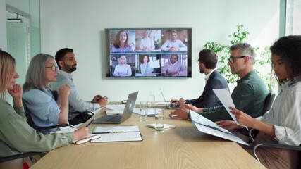 Diverse company employees having online business conference video call on tv screen monitor in board meeting room. Videoconference presentation, global virtual group corporate training concept. - Powered by Adobe