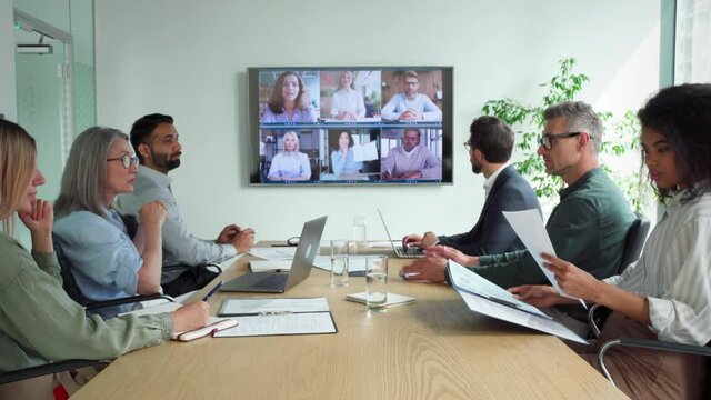 Diverse company employees having online business conference video call on tv screen monitor in board meeting room. Videoconference presentation, global virtual group corporate training concept.
