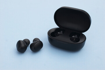 Wireless headphones or earbuds with charging case on bright blue background.