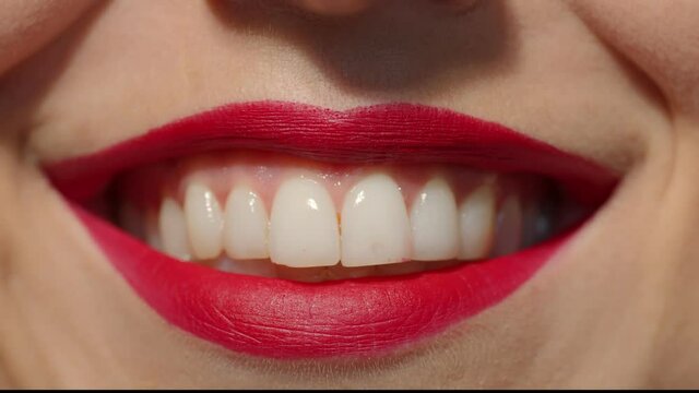 Lips with red lipstick close-up. Caucasian girl with plump lips smiling wide showing white teeth. Anonymous lady studio still shot slow motion.