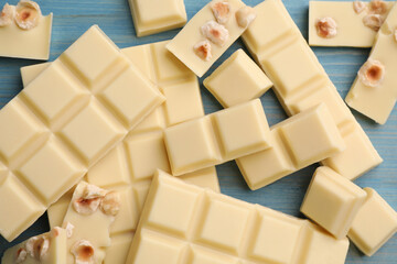 Delicious white chocolate with hazelnuts on light blue wooden table, flat lay