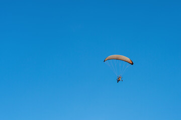 A powered paraglider trike flying over clear blue sky back view