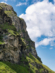 Fototapeta na wymiar In Swiss Alps, rock wall with grass against blue sky with clouds