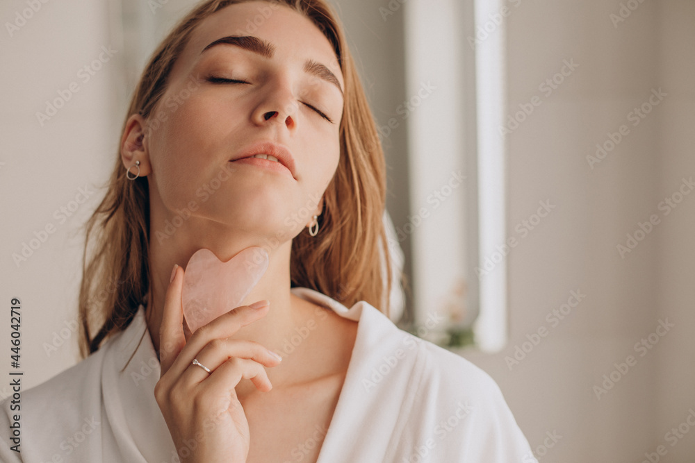 Wall mural Woman doing self massage with rose quartz gua sha stone