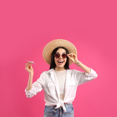 Happy female tourist with toy plane on pink background