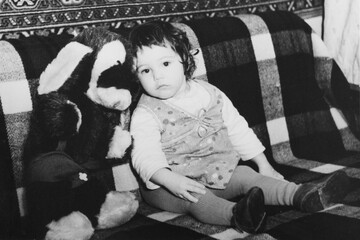 Vintage photo of little girl with a toy dog. Early 1980s. Old surface, soft focus. Transferred property, family archive.