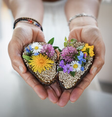 woman holding vegan halved avocado heart decorated with daisy, dandelion and meadow flowers for a healthy snack
