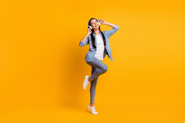Fototapeta na wymiar Full size photo of cool optimistic brunette lady listen music wear blue shirt jeans sneakers isolated on yellow color background