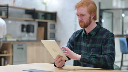 Young Redhead Man using Digital Tablet in Cafe 