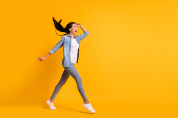 Fototapeta na wymiar Full size profile photo of cool optimistic brunette lady go look wear blue shirt jeans sneakers isolated on yellow color background