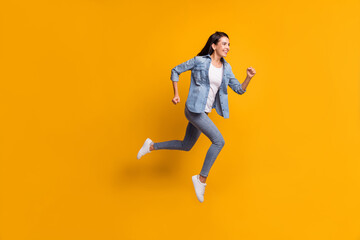 Fototapeta na wymiar Full size profile photo of cool optimistic brunette lady run jump wear blue shirt jeans sneakers isolated on yellow color background