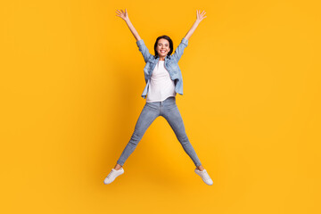 Fototapeta na wymiar Full size photo of nice optimistic brunette lady jump wear blue shirt jeans sneakers isolated on yellow background