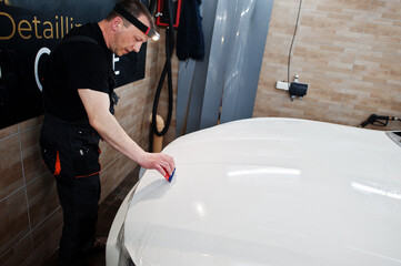 Worker in detailing garage put polyurethane anti-gravel film cover in white luxury car.