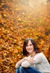 Autumn portrait of attractive young brunette woman sitting in autumn forest