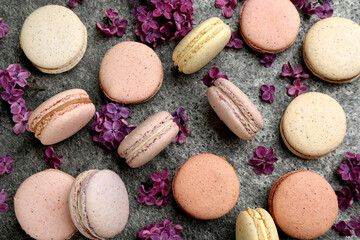 Delicious macarons and flowers on grey table, flat lay