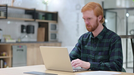 Young Redhead Man in Cafe using Laptop 