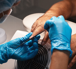 Nail master makes a manicure for man. Close-up of hand in blue gloves and man's brutal hand