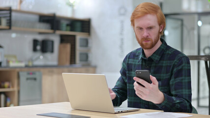 Redhead Man working on Smartphone and Laptop 