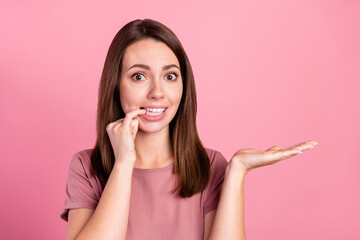 Photo of impressed unsure woman dressed casual clothes arm holding empty space biting finger isolated pink color background