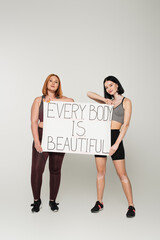 Body positive sportswomen holding placard with every body is beautiful lettering on grey background