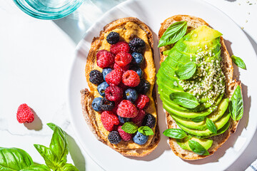 Peanut butter and berries toast and avocado toast with basil on white plate. Healthy vegan...