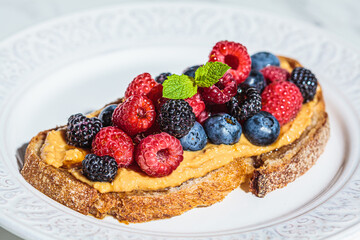 Toast with peanut butter and berries on white plate. Healthy vegan breakfast concept.