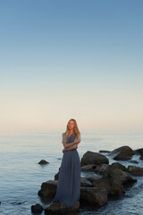 beautiful girl in a gray dress by the sea at sunset