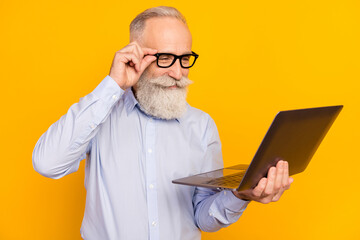 Photo of concentrated old charming man look laptop smile wear glasses isolated on yellow color...
