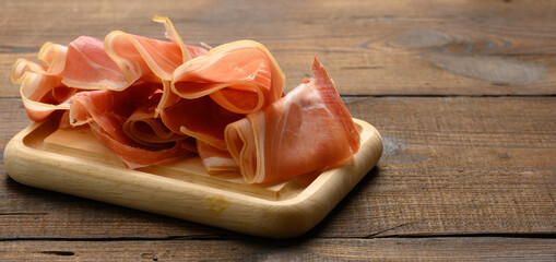 sliced thin slices of prosciutto on wooden brown board