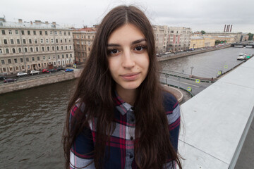 portrait of an Armenian girl with fluttering long black hair in a checkered shirt and jeans on a rooftop in the center of St. Petersburg