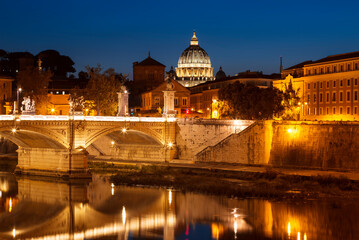 Fototapeta na wymiar View of Rome at night with the vittorio emanuele II bridge, the dome of St. Peter's Cathedral and their reflection in the water of the Tiber river late in the evening. Italy