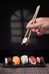 Hand picking sushi variety with chopsticks on dark background. Vertical format.